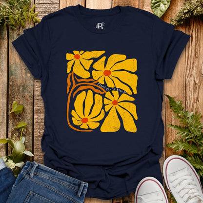 Navy blue t-shirt with yellow floral design on a wooden surface with plants.