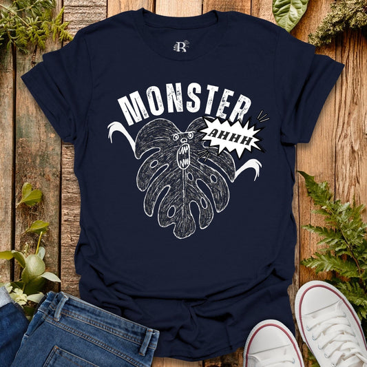 Navy blue t-shirt with a graphic design of a monster and text on a wooden surface with plants.