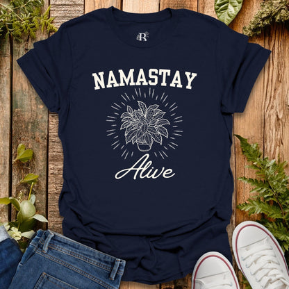Navy blue t-shirt with 'Namastay Alive' design on a wooden surface with plants.