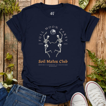 Navy blue t-shirt with skeleton design and text on a wooden surface with plants.