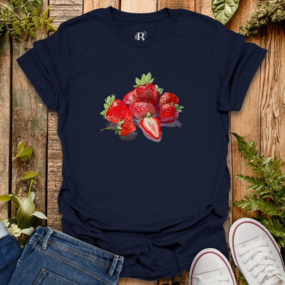 Navy blue t-shirt with strawberry design on a wooden surface with jeans and white sneakers.