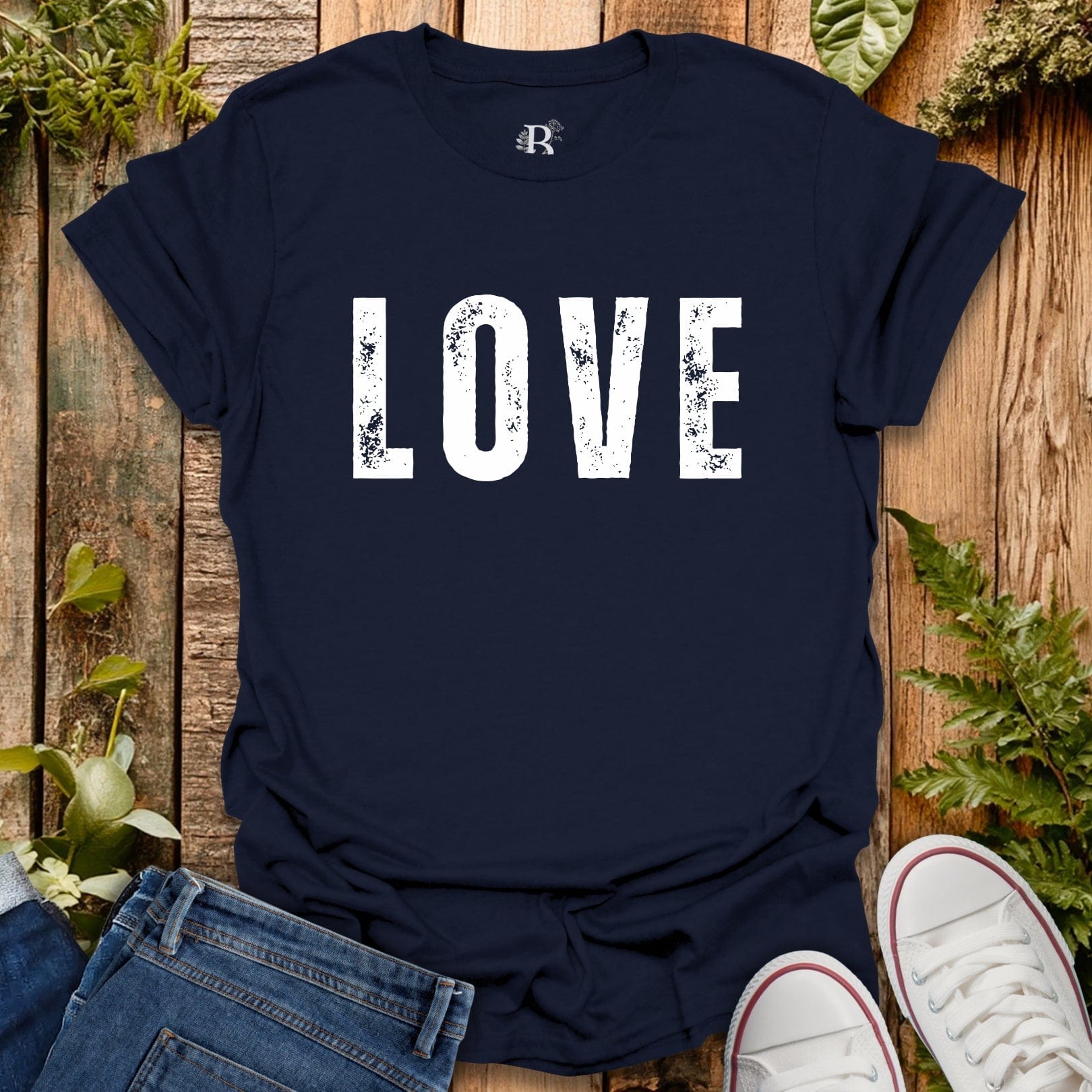 Navy blue t-shirt with 'LOVE' printed on it, placed on a wooden surface with jeans and white sneakers.