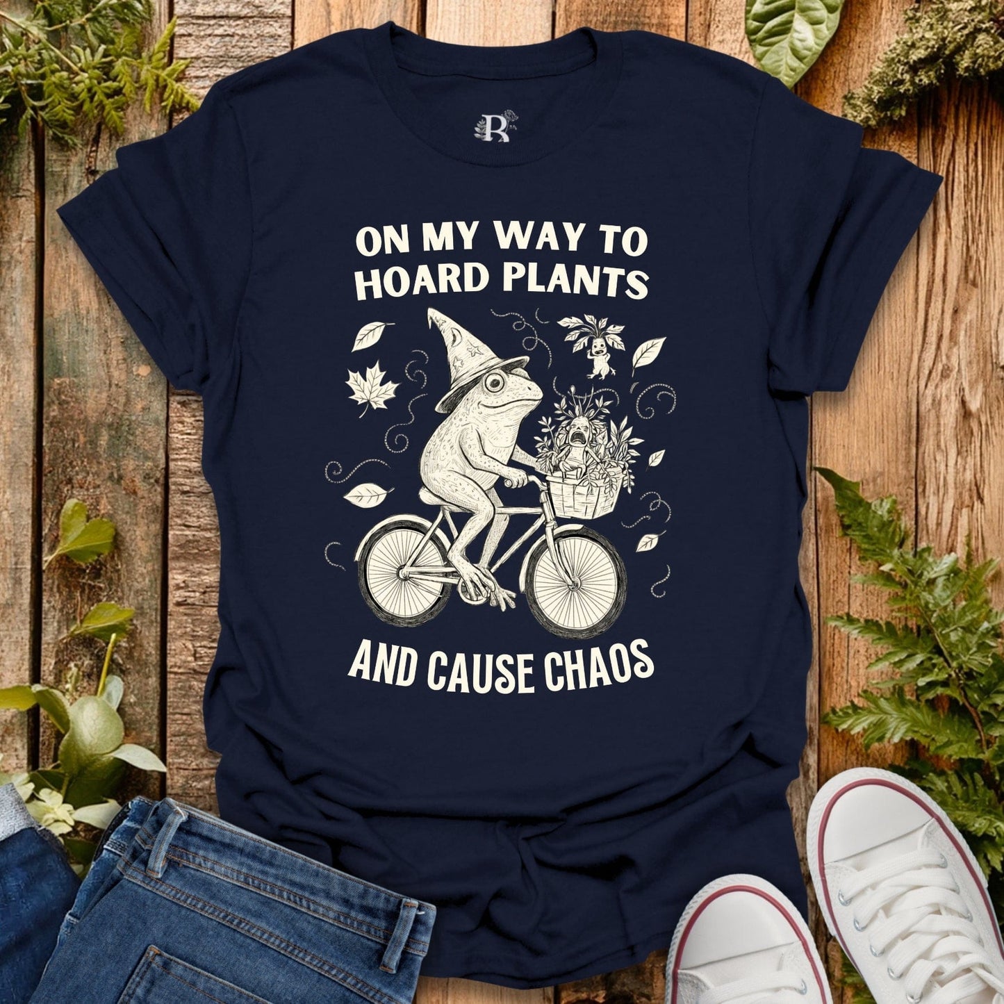 Navy blue t-shirt with a graphic of a frog riding a bike and text on a wooden background with plants.