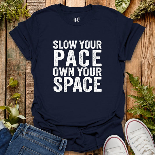 Navy blue t-shirt with 'Slow your pace, own your space' text on a wooden background