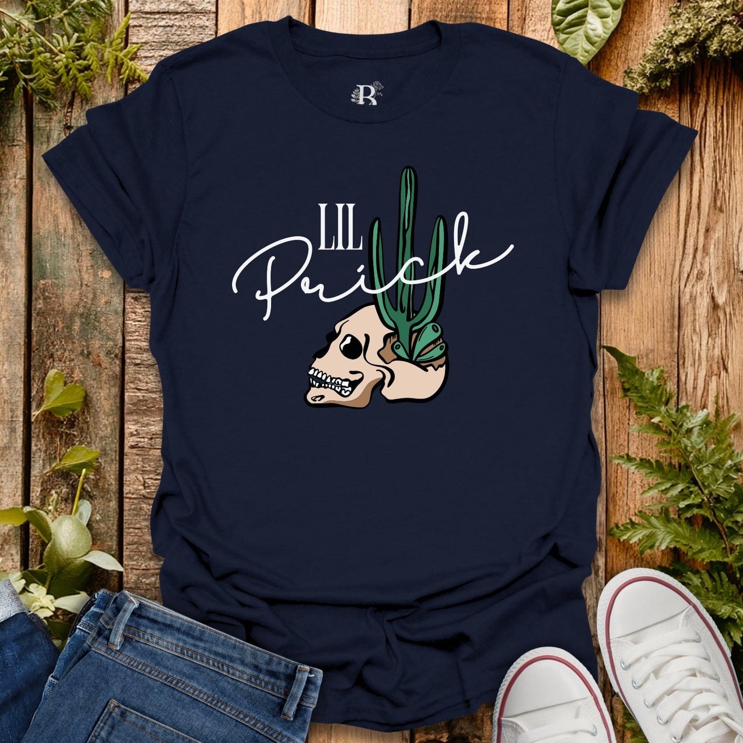 Navy blue t-shirt with skull and cactus design on a wooden surface with plants.