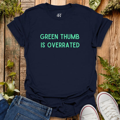 Navy blue t-shirt with 'Green Thumb is Overrated' text on a wooden surface with plants.