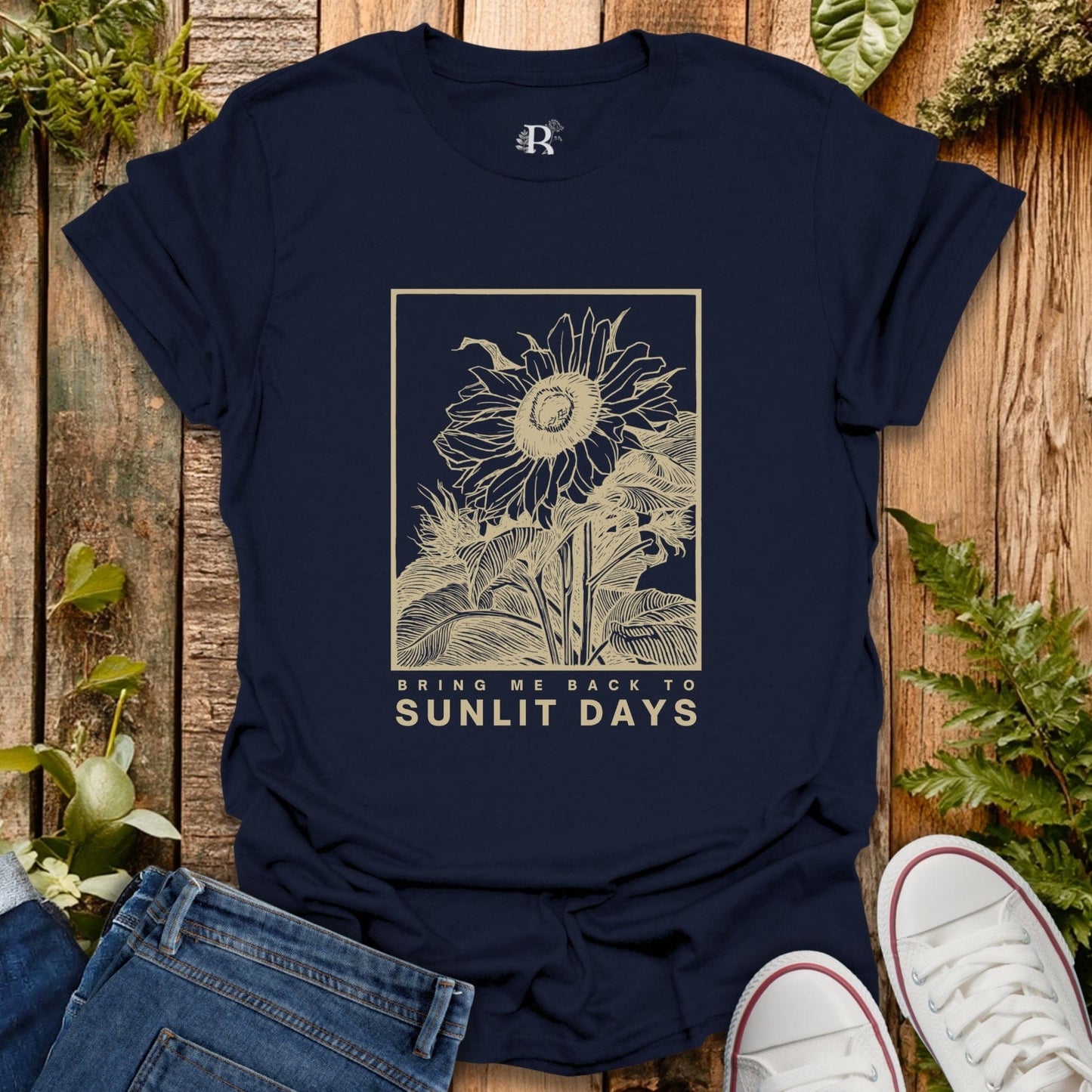 Navy blue t-shirt with sunflower design and text on a wooden surface with plants.