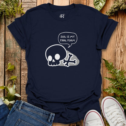 Navy blue t-shirt with skull design and 'soil is my final form' text on a wooden surface with plants.