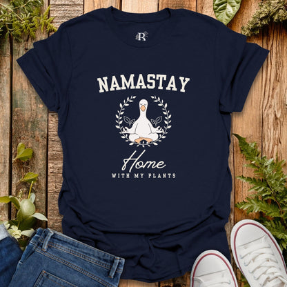 Navy blue t-shirt with 'Namastay Home with My Plants' design on a wooden surface with plants.