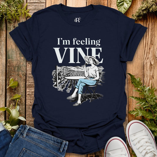 Navy blue t-shirt with 'I'm feeling VINE' graphic on a wooden surface with plants.