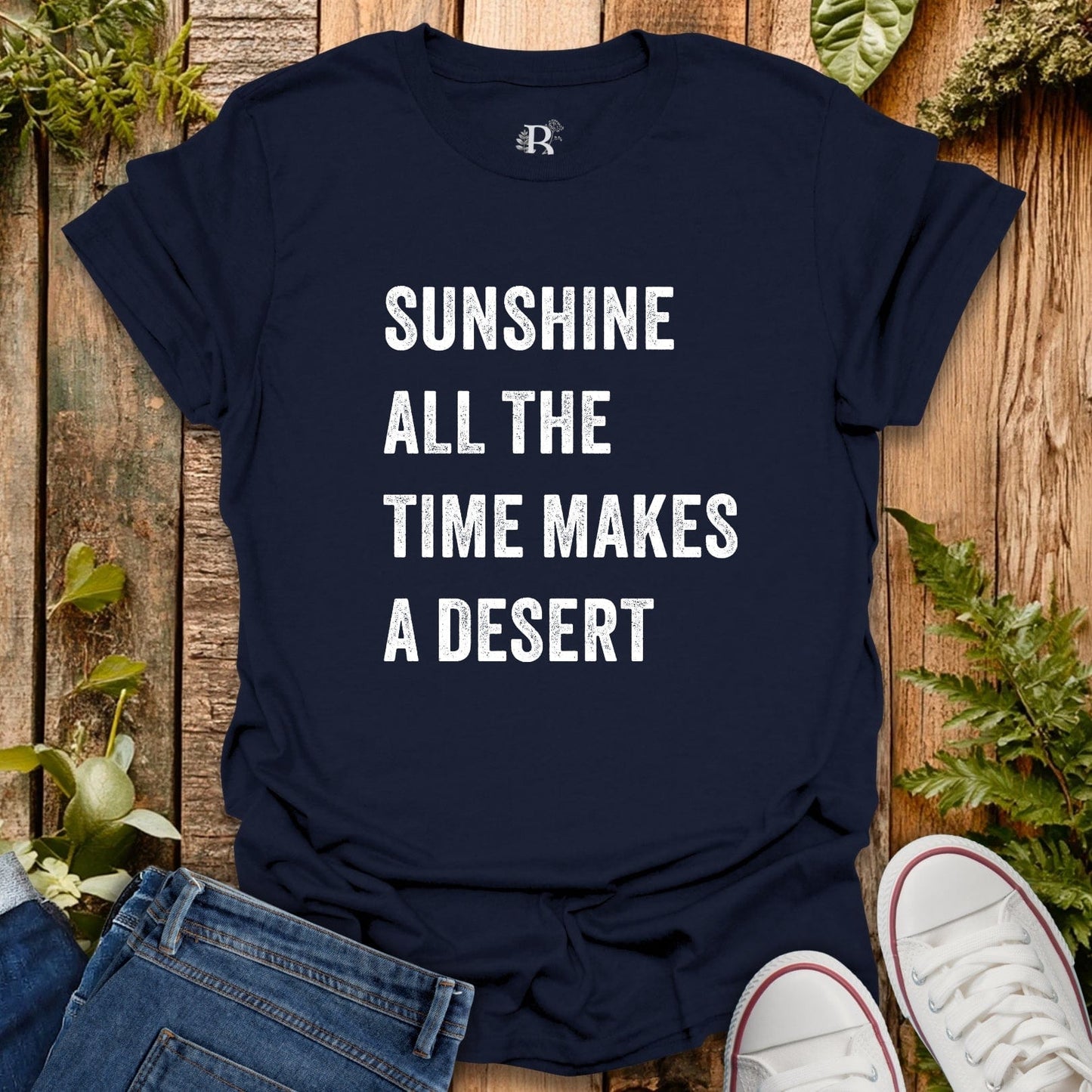 Navy blue t-shirt with humorous text on a wooden surface with plants.