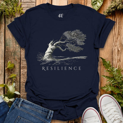 Navy blue t-shirt with 'Resilience' graphic design on a wooden surface with plants.