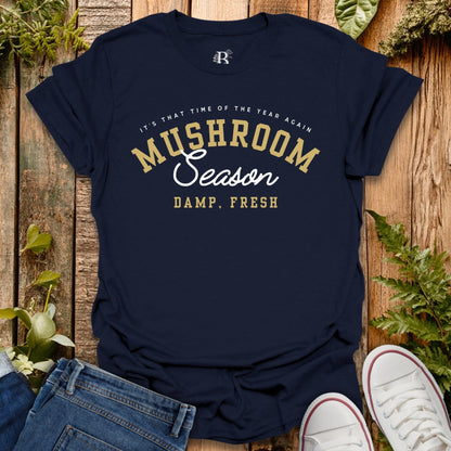 Navy blue t-shirt with yellow and white text on a wooden surface with plants.