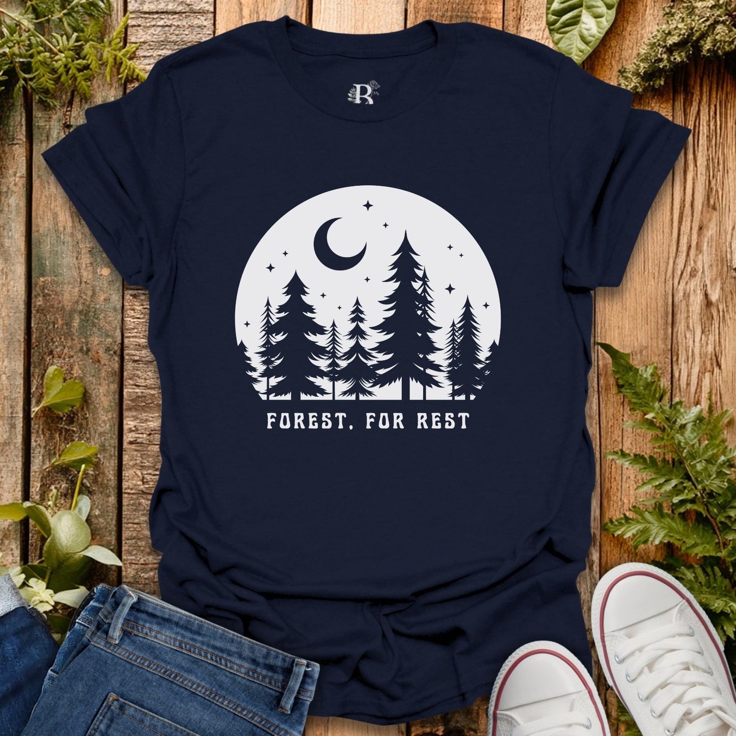 Navy blue t-shirt with 'Forest, For Rest' design on a wooden surface with plants.