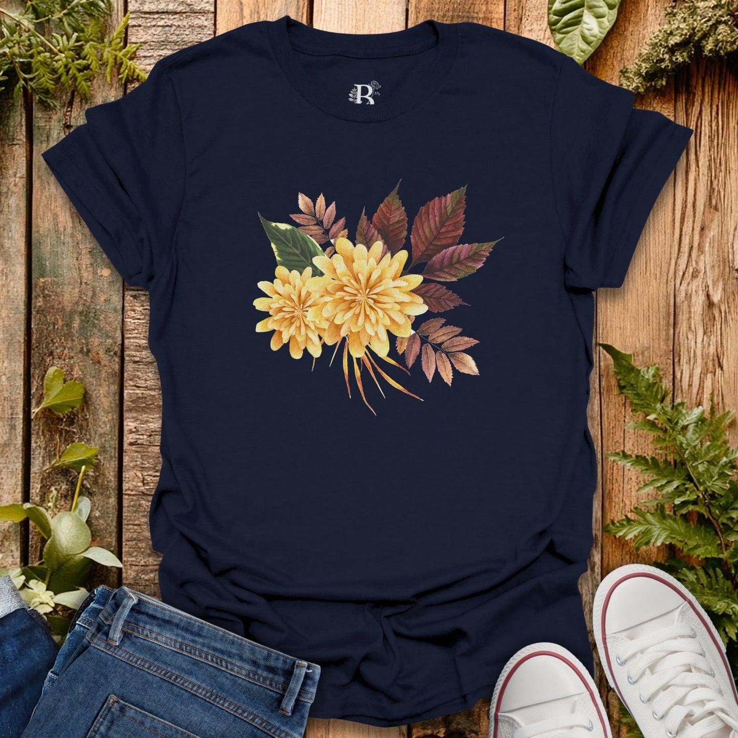 Navy blue t-shirt with yellow floral design on a wooden surface with plants.