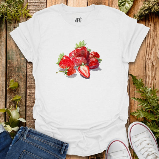 White t-shirt with strawberry design on a wooden surface with plants.