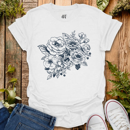 White t-shirt with floral design on a wooden surface with plants.
