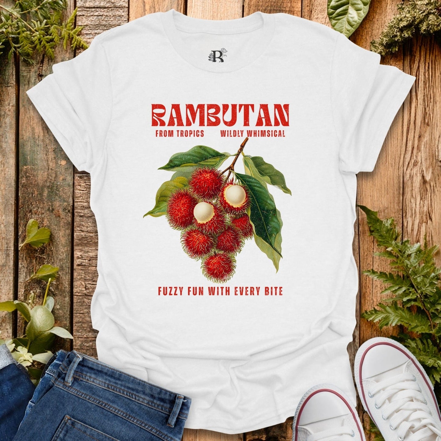 White t-shirt with rambutan graphic and text on a wooden surface with plants.
