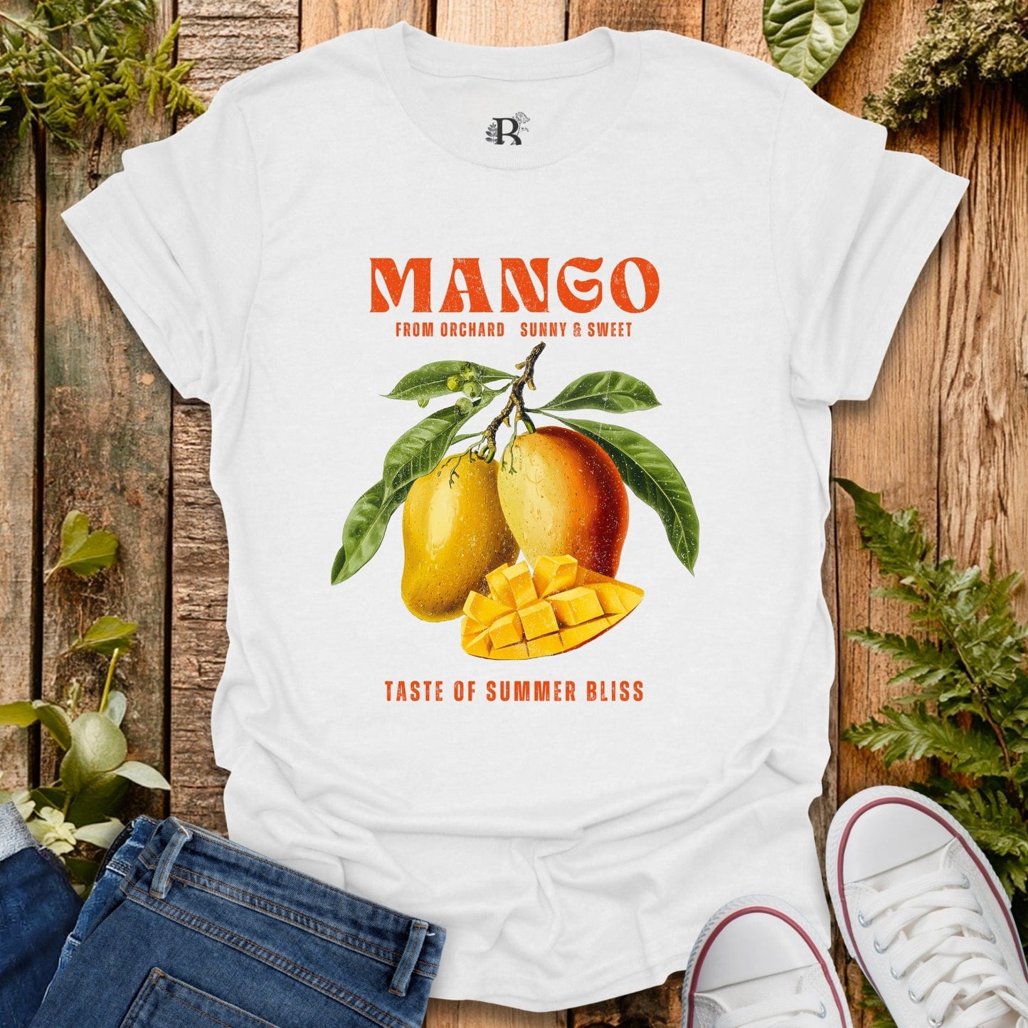 White t-shirt with mango graphic and text on a wooden surface with plants.