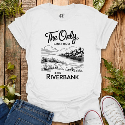 White t-shirt with black graphic and text on a wooden surface with plants