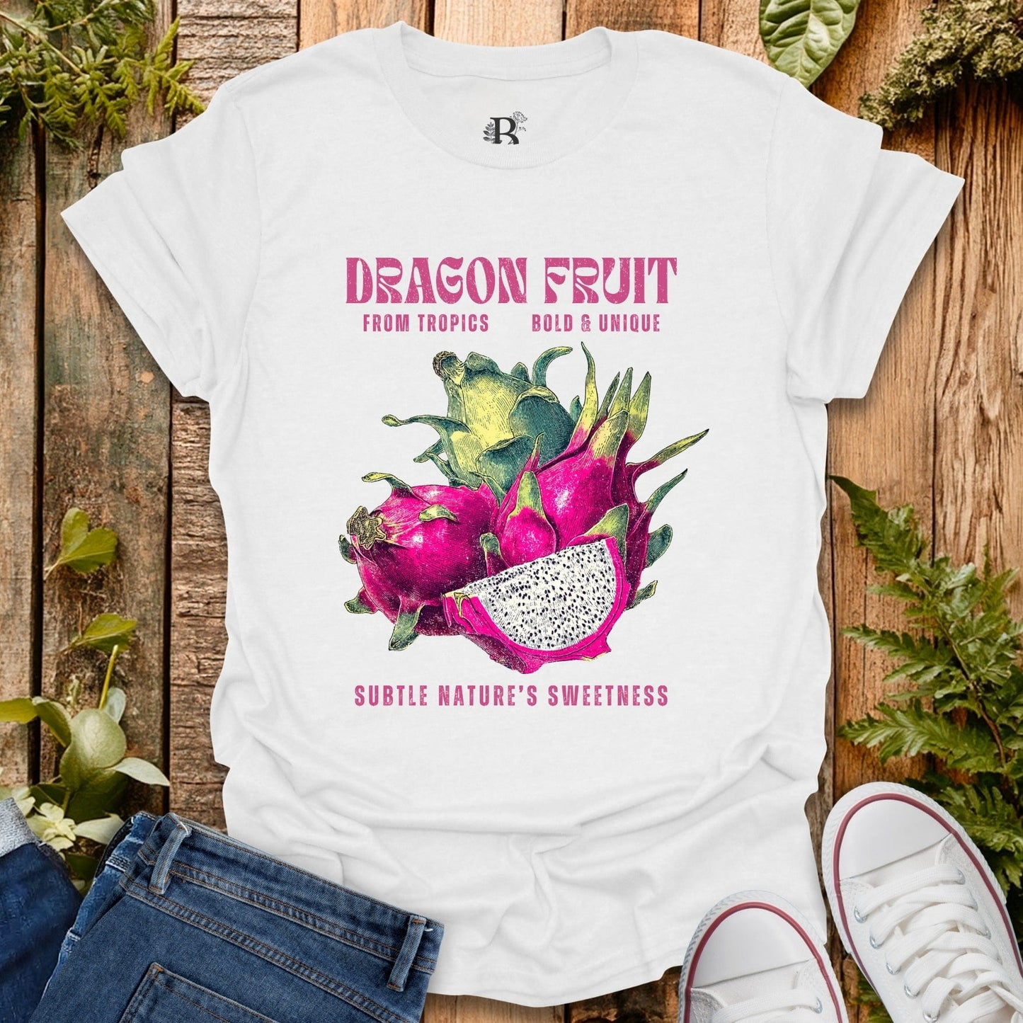 White t-shirt with dragon fruit graphic and text on a wooden surface with plants.