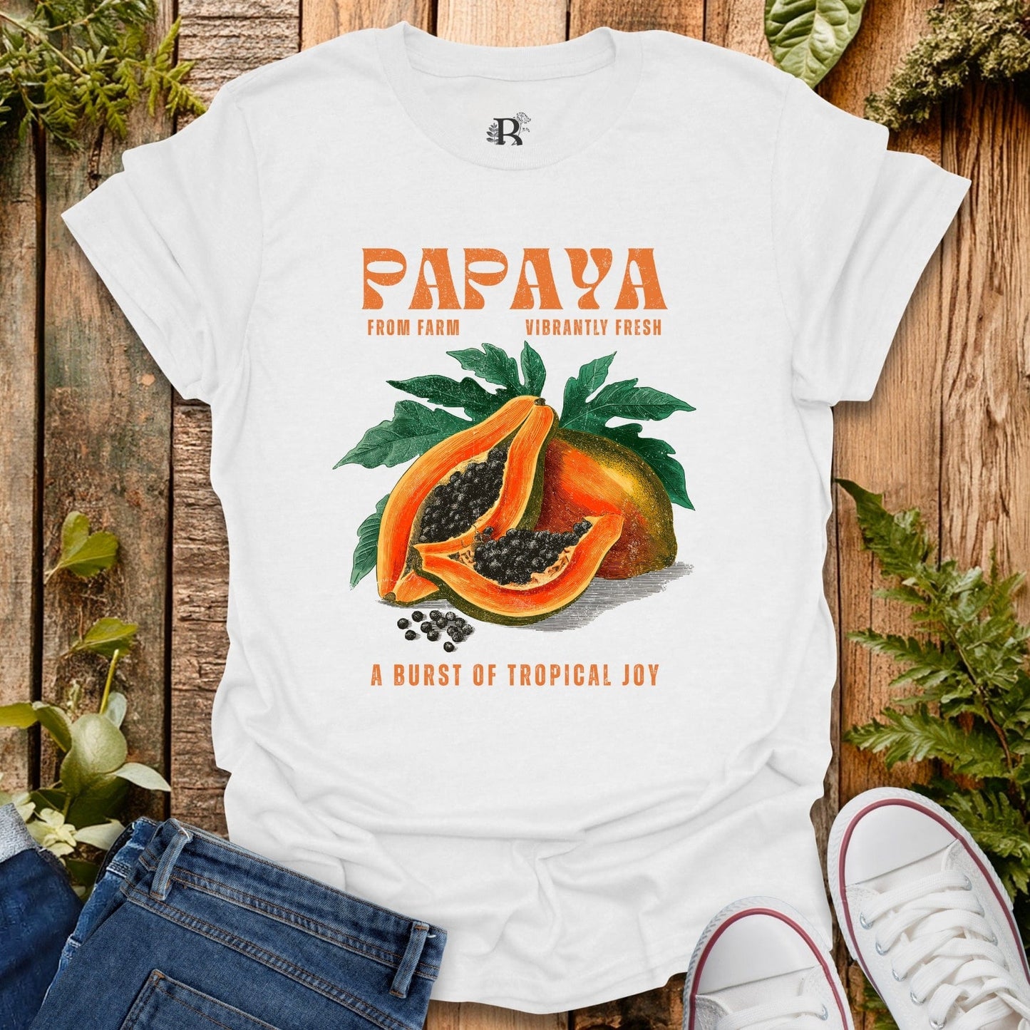 White t-shirt with papaya graphic and text on a wooden surface with plants.