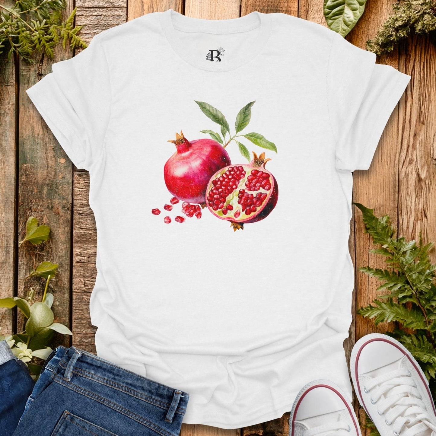 White t-shirt with pomegranate design on a wooden surface with plants.