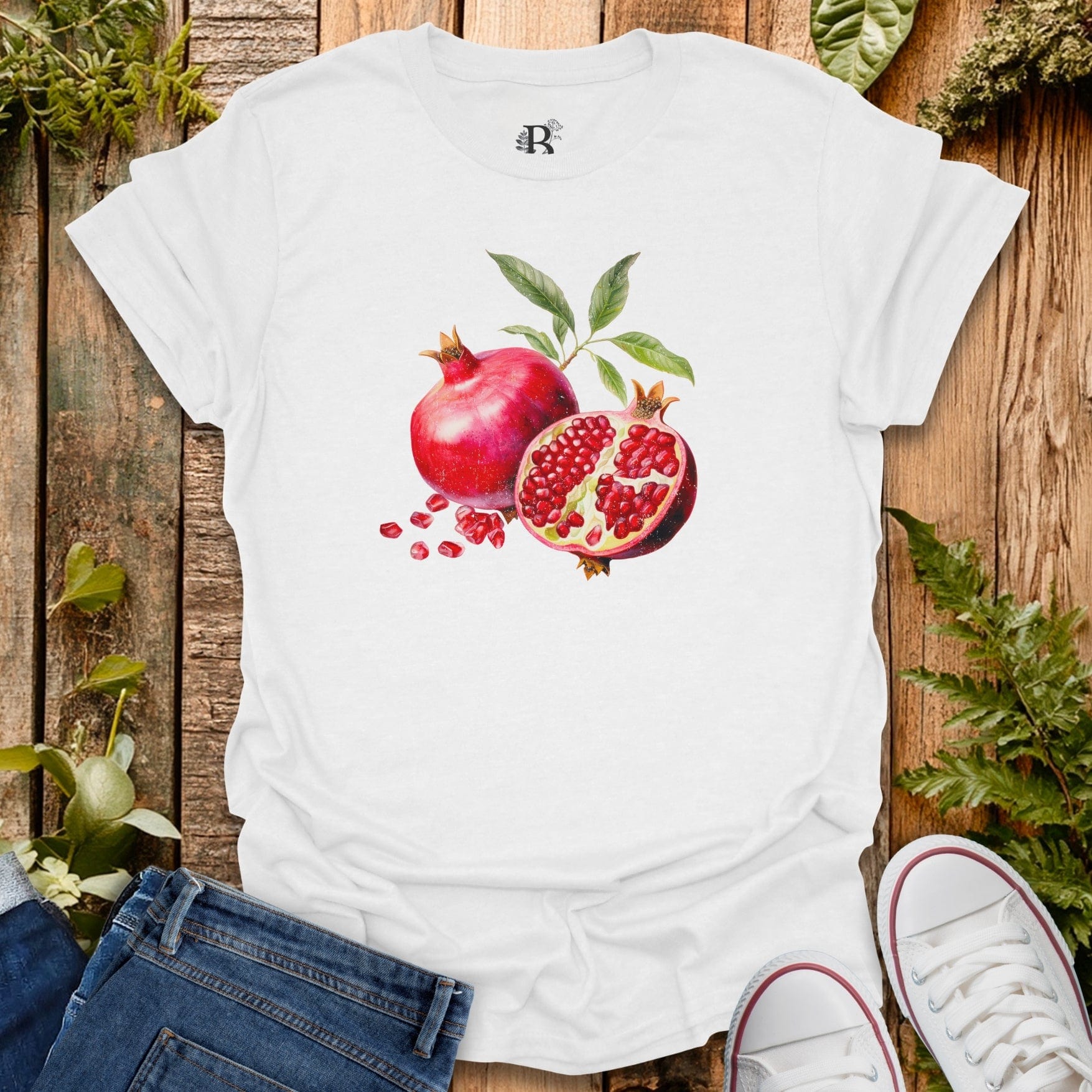 White t-shirt with pomegranate design on a wooden surface with plants.