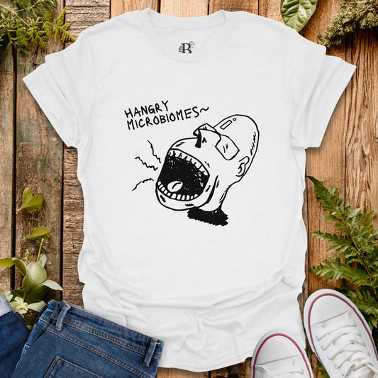 White t-shirt with a graphic design and text on a wooden surface with plants.