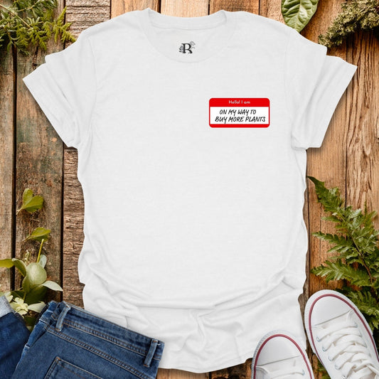 White t-shirt with a red name tag graphic and text on a wooden surface with plants.