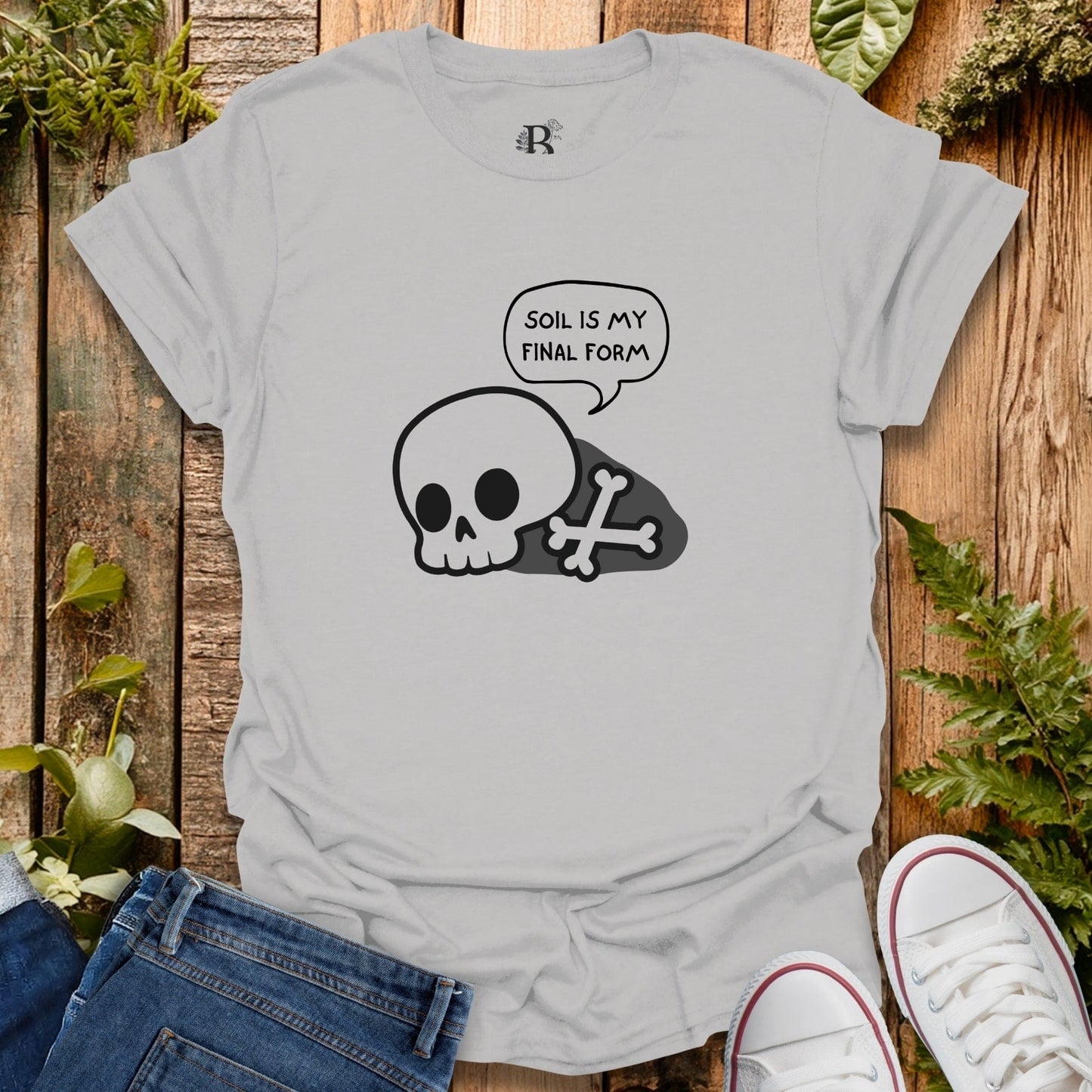 Gray t-shirt with skull and crossbones design and 'SOIL IS MY FINAL FORM' text on a wooden background.