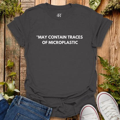 Black t-shirt with 'MAY CONTAIN TRACES OF MICROPLASTIC' text on a wooden surface with jeans and white sneakers.