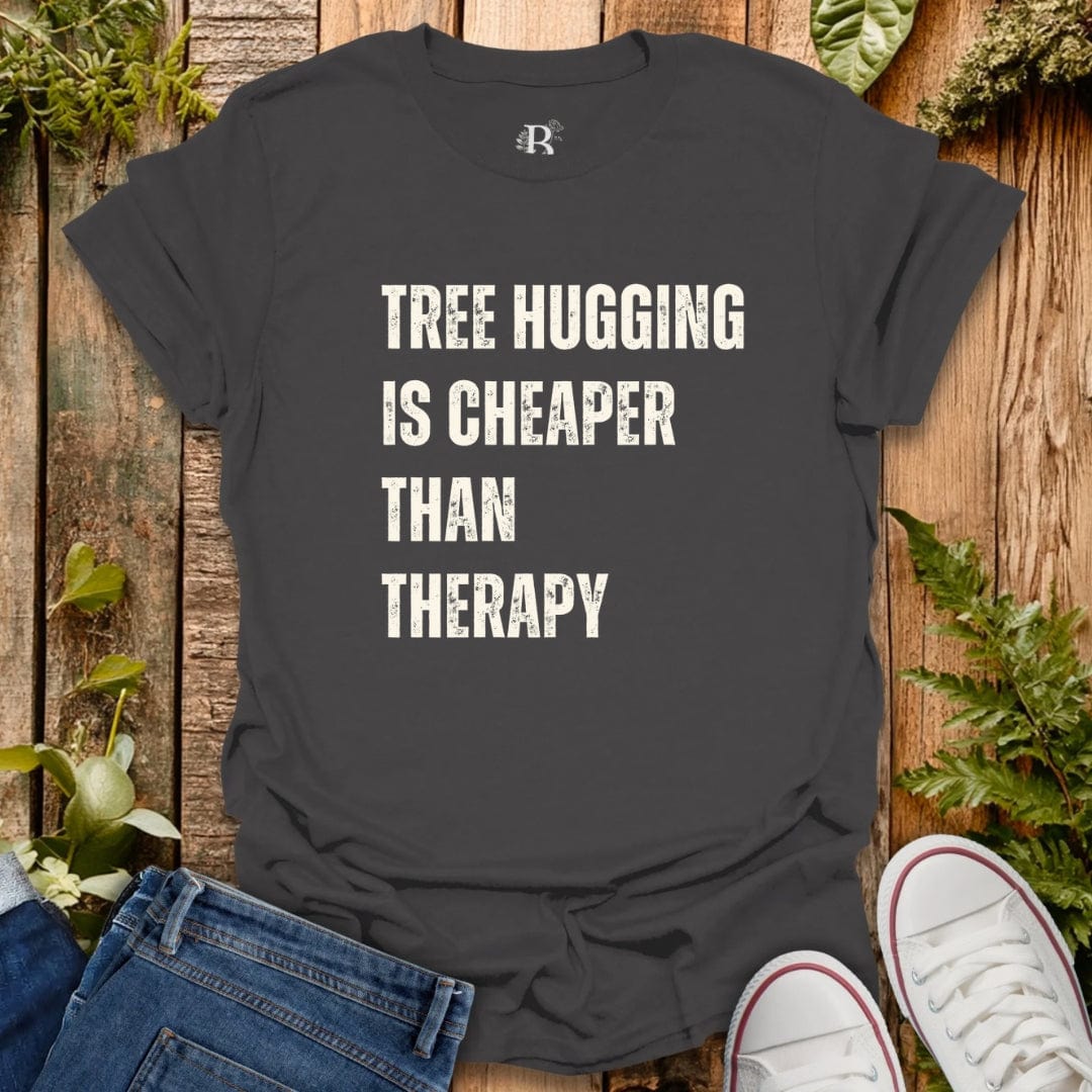 Black t-shirt with 'Tree Hugging is Cheaper Than Therapy' text on a wooden background with plants.