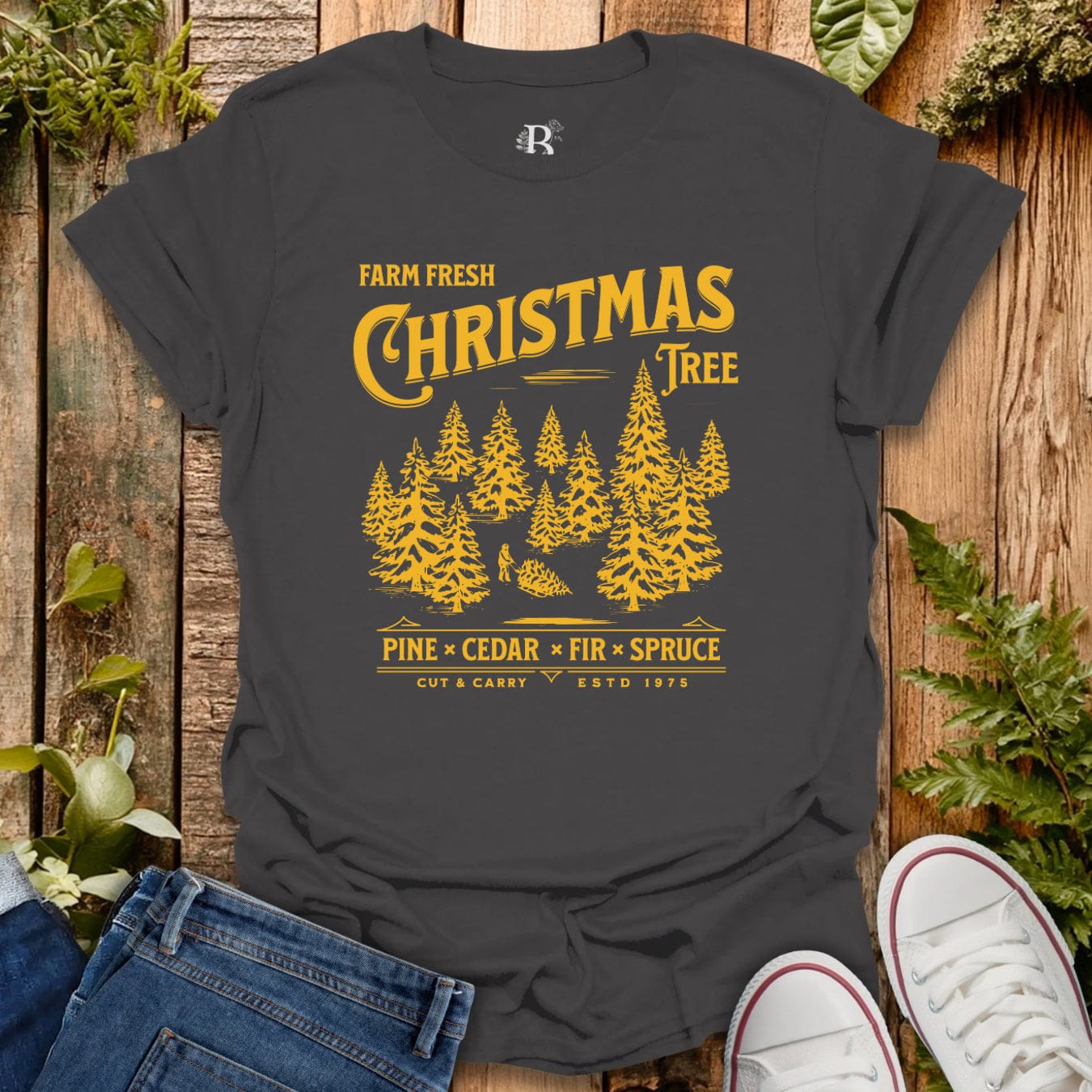Dark gray t-shirt with yellow Christmas tree design on a wooden surface with plants.