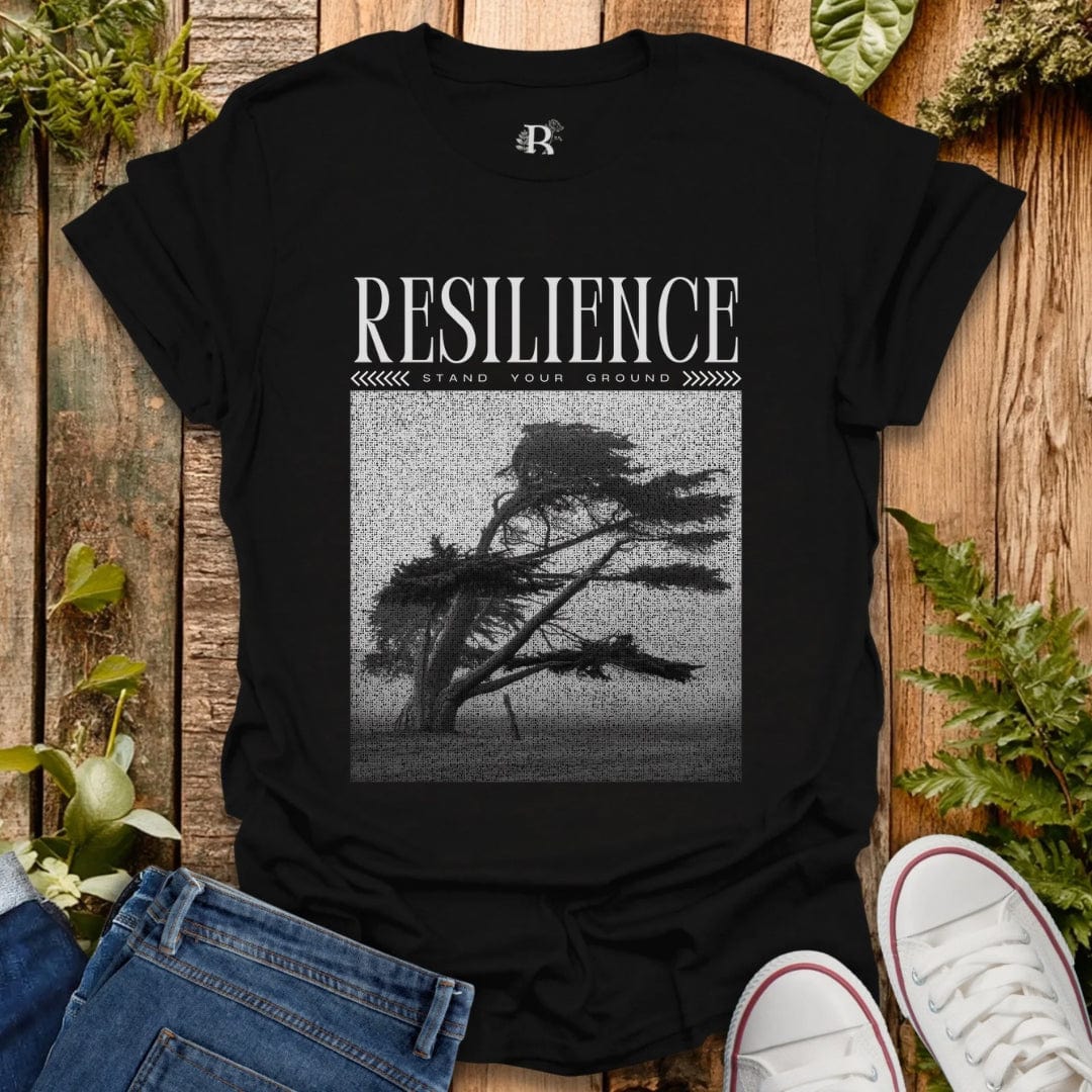 Black t-shirt with 'Resilience' graphic and text on a wooden surface with plants.