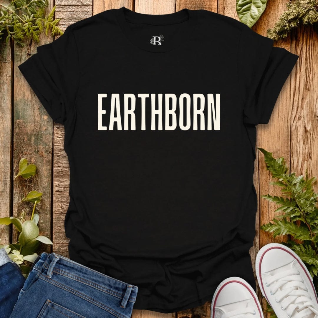 Black t-shirt with 'EARTHBORN' text on a wooden surface with plants.