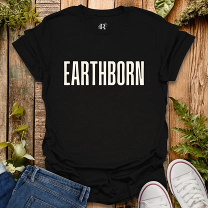 Black t-shirt with 'EARTHBORN' text on a wooden surface with plants.