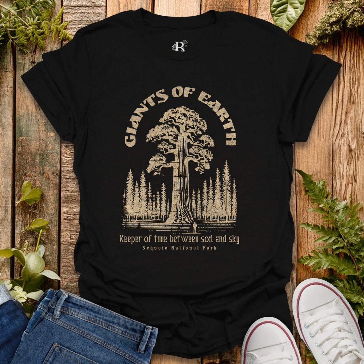 Black t-shirt with 'Giants of Earth' graphic design on a wooden surface with plants.