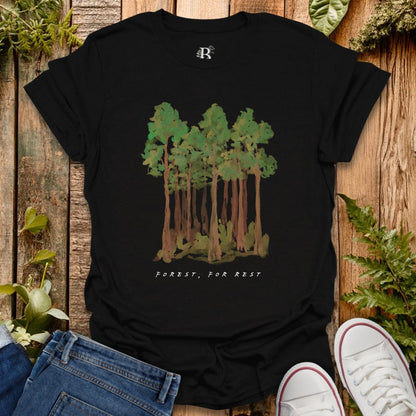 Black t-shirt with forest graphic and text on a wooden surface with plants.