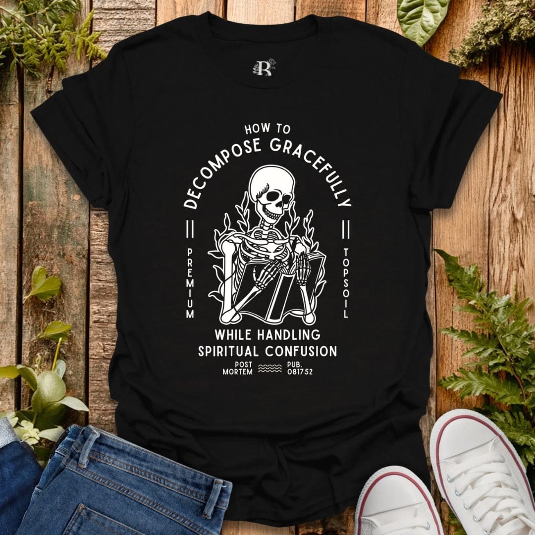 Black t-shirt with a white graphic design on a wooden surface with plants.