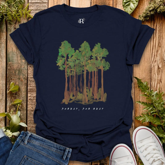 Navy blue t-shirt with forest graphic and 'Forest, For Rest' text on a wooden surface with plants.