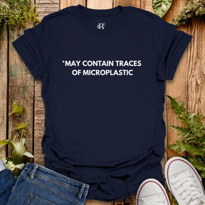 Navy blue t-shirt with text 'MAY CONTAIN TRACES OF MICROPLASTIC' on a wooden surface with jeans and white sneakers.