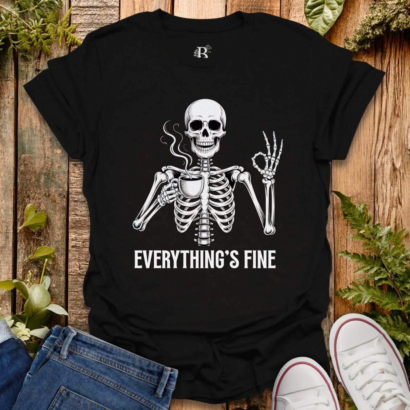 Black t-shirt with a skeleton graphic and 'Everything's Fine' text on a wooden surface with plants.