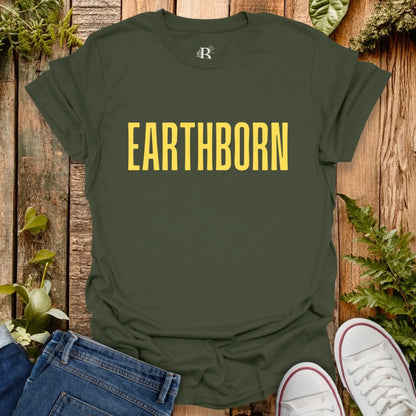Green t-shirt with 'EARTHBORN' text on a wooden background with plants.