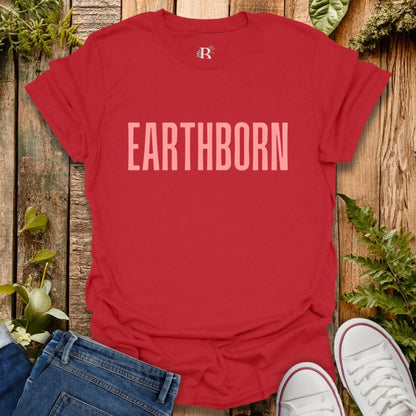 Red t-shirt with 'EARTHBORN' text on a wooden surface with plants.