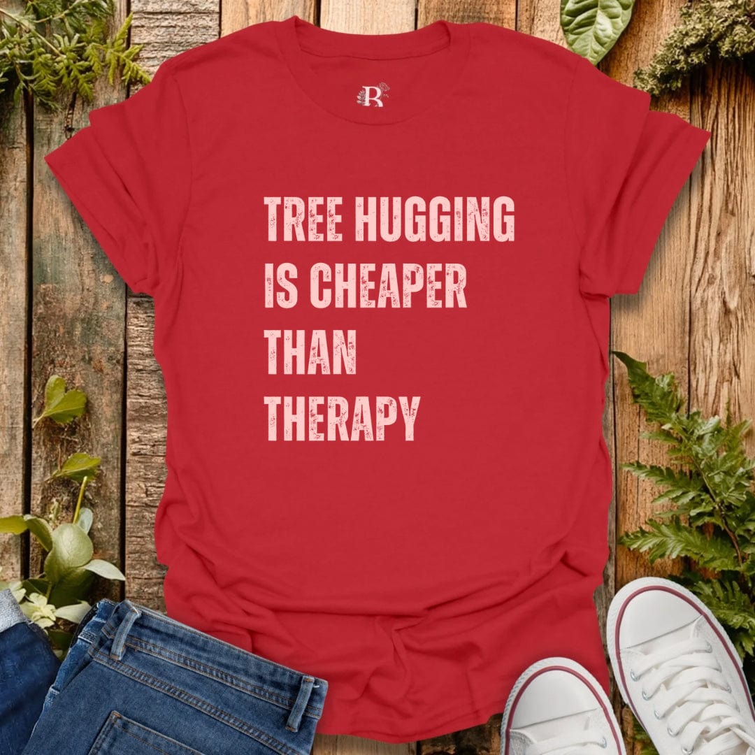 Red t-shirt with 'Tree Hugging is Cheaper Than Therapy' text on a wooden background with plants.