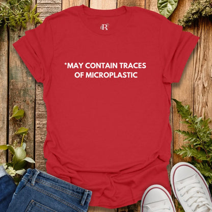 Red t-shirt with text 'MAY CONTAIN TRACES OF MICROPLASTIC' on a wooden surface with plants.