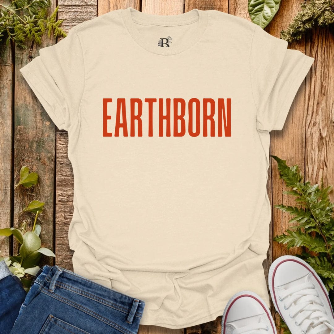Beige t-shirt with 'EARTHBORN' text on a wooden background with plants.