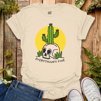 Beige t-shirt with a cactus and skull design and 'Everything's Fine' text on a wooden background.