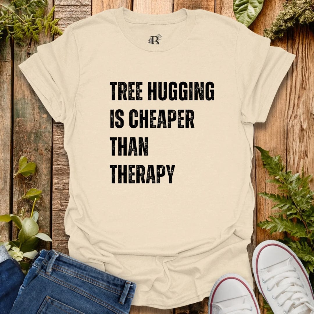 Beige t-shirt with 'Tree Hugging is Cheaper Than Therapy' text on a wooden background with plants.